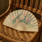 Photographie réaliste d'un éventail en soie posé sur une chaise en rotin, style Berthe Morisot